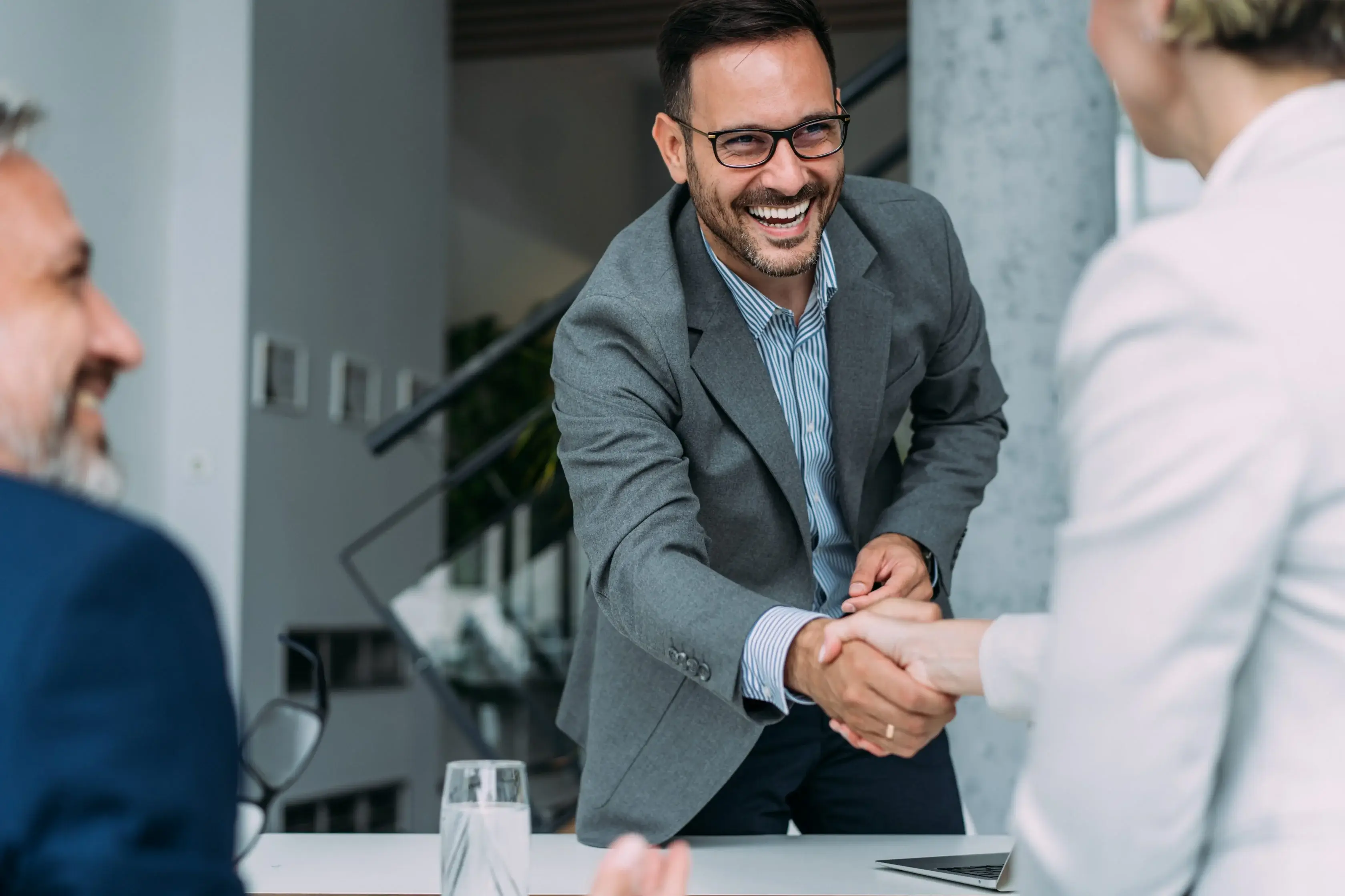 Businessman shaking hands with colleagues in a modern office setting, symbolizing collaboration and partnership.