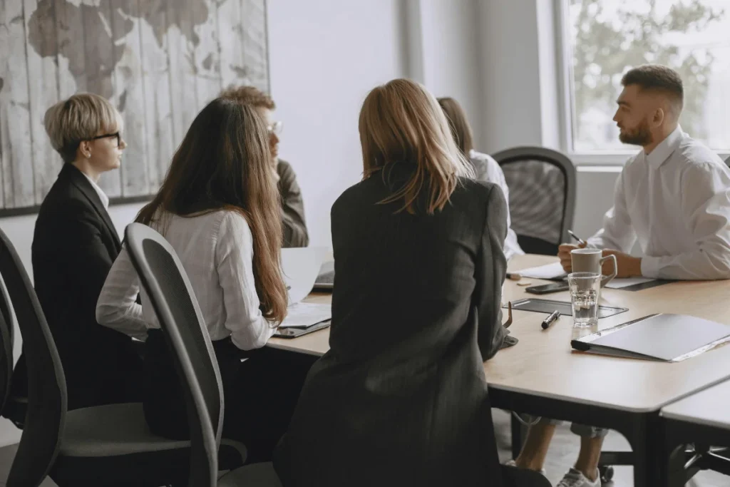 A group of professionals seated around a conference table, engaging in a business meeting with documents and drinks in front of them.