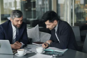 Two businessmen in suits analyzing financial reports with coffee cups.
