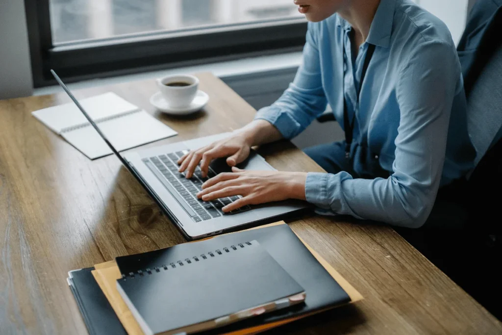 Business professional typing on laptop at wooden desk.