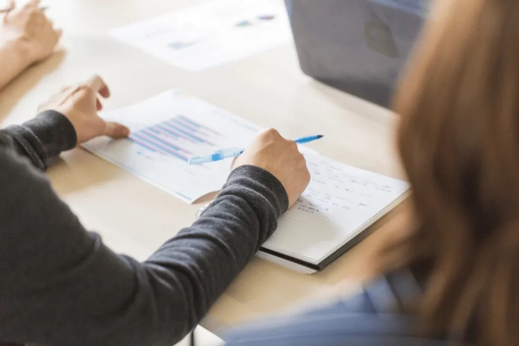 Professional taking meeting notes while reviewing business chart.