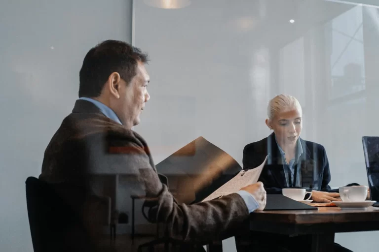 A man and woman in a business meeting at a table with documents and laptops.