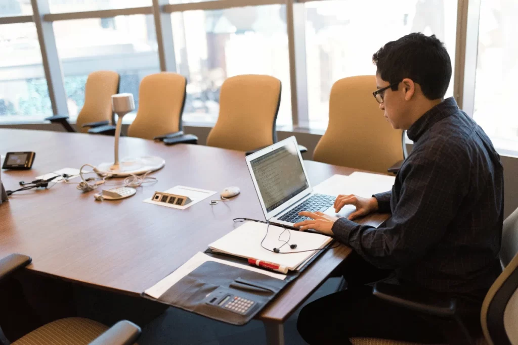 Business professional working on a laptop alone in a large conference room.