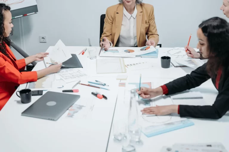 A diverse group of professionals collaborates around a conference table, analyzing documents and discussing strategies.