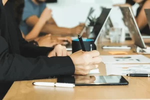 Person holding pen and notebook while collaborating with team in office.