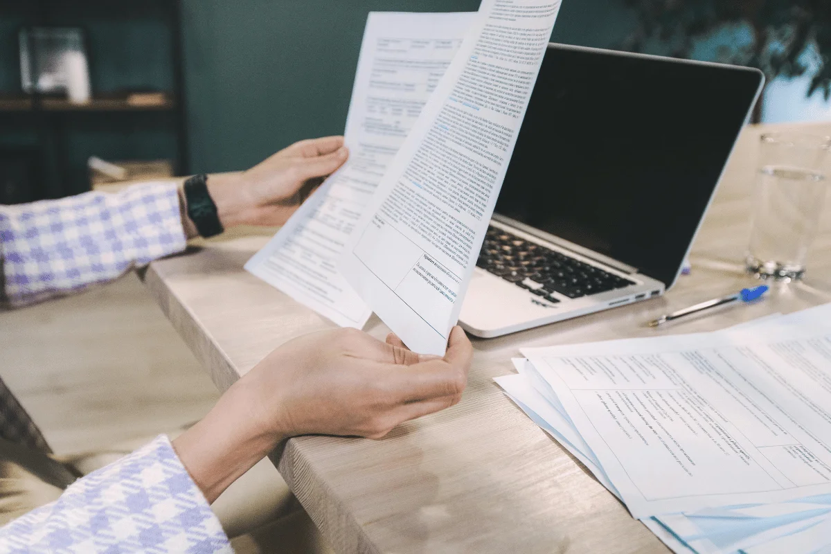 Business professional reviewing financial documents beside a laptop.