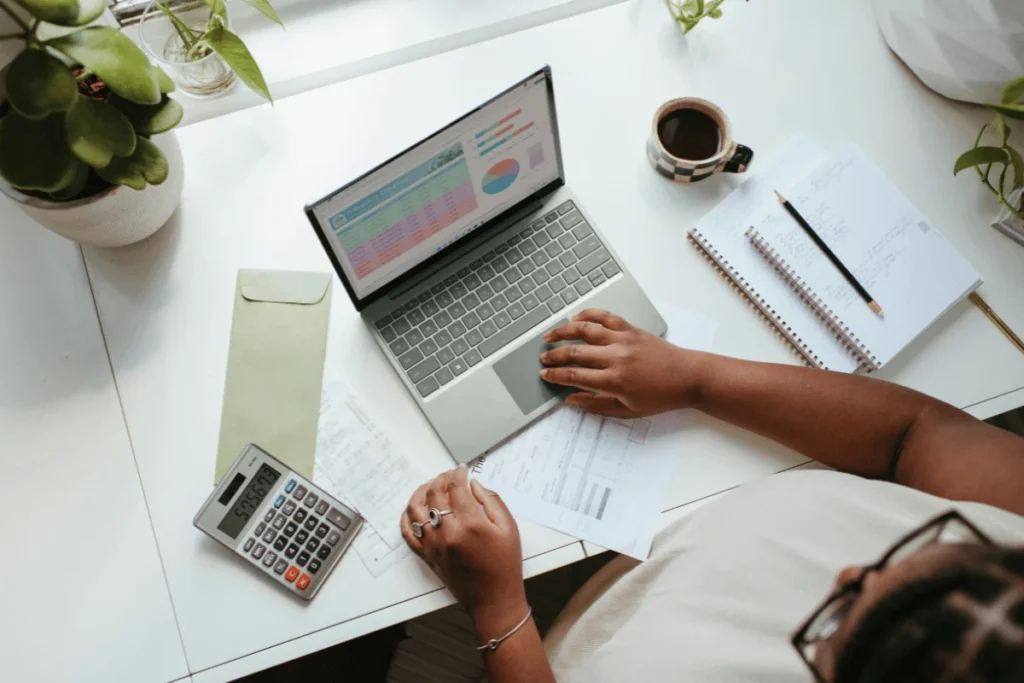 Businesswoman reviewing financial data on laptop while calculating expenses.