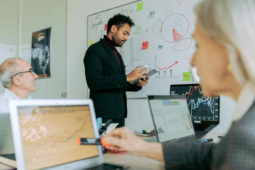 Man presenting financial data on a whiteboard while colleagues review graphs.