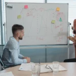Two professionals reviewing technology integration strategy on whiteboard in modern office.