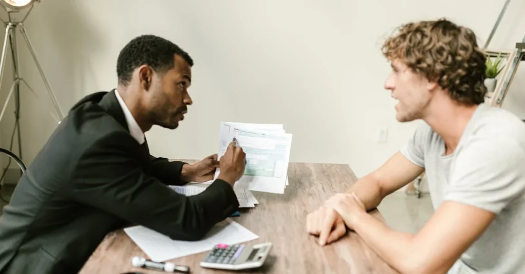 Business consultant discussing paperwork with a client at a desk with documents and a calculator.