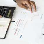 Person using calculator and analyzing software industry integration savings charts on desk.