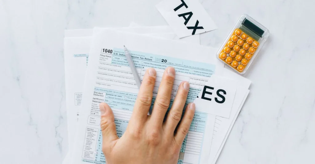Hand on tax forms with calculator on white desk.