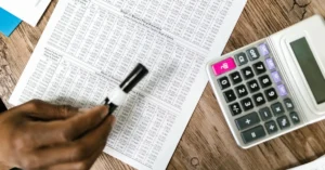 Hand holding pen over tax forms with calculator on wooden desk showing alternative minimum tax Canada calculations