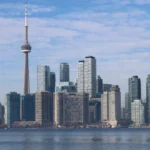 Toronto skyline with CN Tower and downtown skyscrapers reflected in Lake Ontario water.