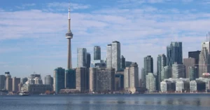 Toronto skyline with CN Tower and downtown skyscrapers reflected in Lake Ontario water.