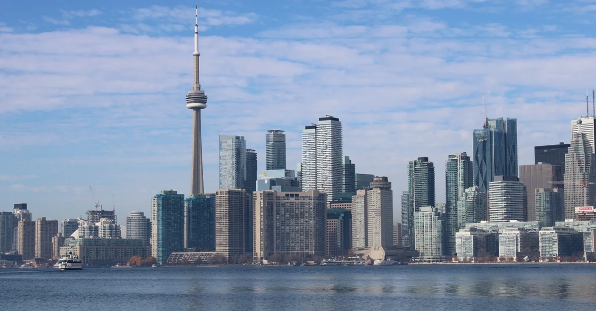 Toronto skyline with CN Tower and downtown skyscrapers reflected in Lake Ontario water.