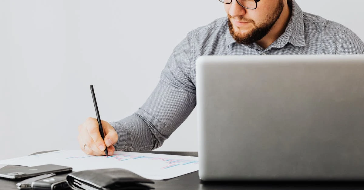 Man in glasses using SaaS valuation calculator on laptop while writing notes at desk.