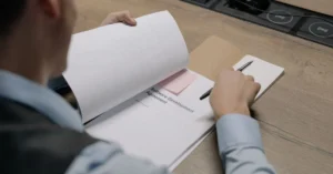 Person reviewing business sale documents and contract terms at desk with printer.