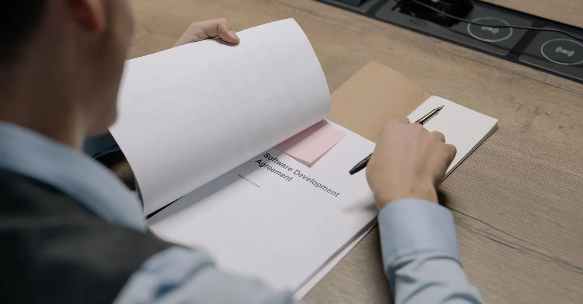 Person reviewing business sale documents and contract terms at desk with printer.