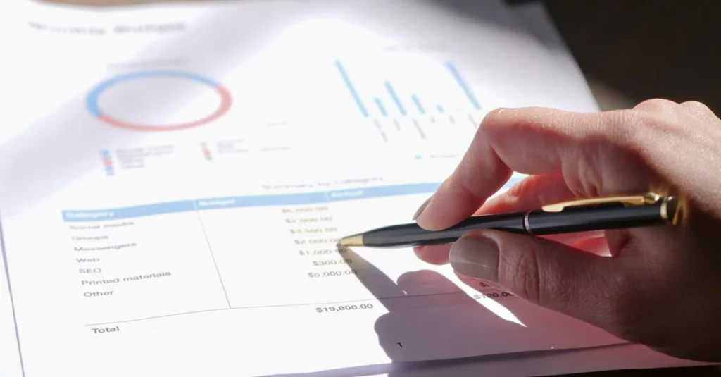 Hand holding pen pointing at financial analysis document with charts and budget data for sell business Ontario transaction.