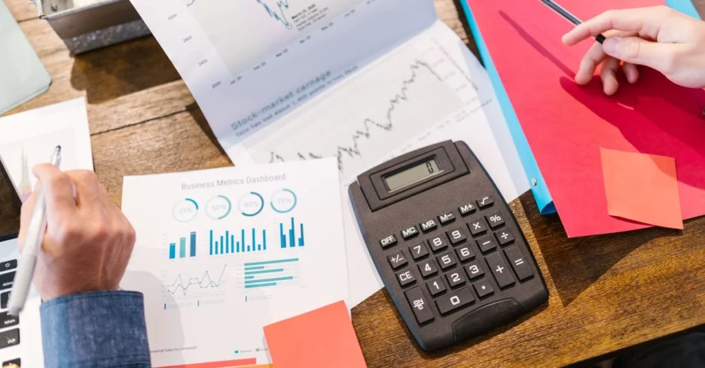Business professional using SaaS valuation calculator with financial charts and graphs on wooden desk.